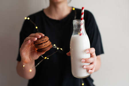 Smiling woman eating chocolate cookies and holding bottle of milk in room close up. Winter holiday season. Good morning.の写真素材