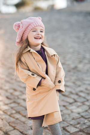 Cute baby girl 3-4 year old wearing knitted hat and beige coat in park outdoors close up. Childhood. Autumn season.の写真素材