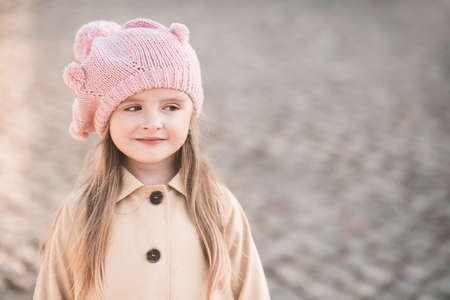 Cute baby girl 3-4 year old wearing knitted hat and beige coat in park outdoors close up. Childhood. Autumn season.の写真素材