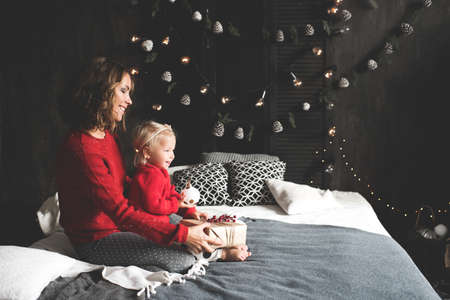 Mother holding baby girl 1-2 year old wearing red knitted sweaters over Christmas decor in room....