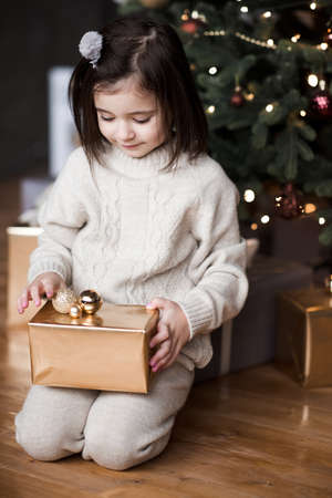 Smiling child girl 4-5 year old sitting under Christmas tree with decorations in room close up. New Year. Winter holiday season.の写真素材
