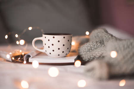 Cup of coffee staying on open book with kitted textile in bed close up. Good morning. Wnter holiday season.の写真素材