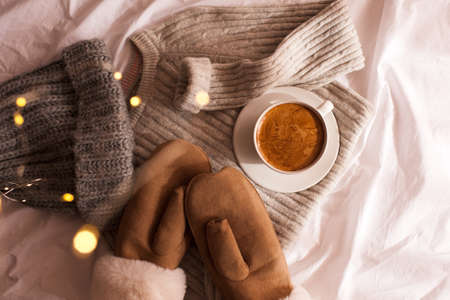 Winter clothes: knitted hat, mittens, woolen sweater and cup of coffee in bed closeup. Top view. Good morning. Winter holiday season.の写真素材