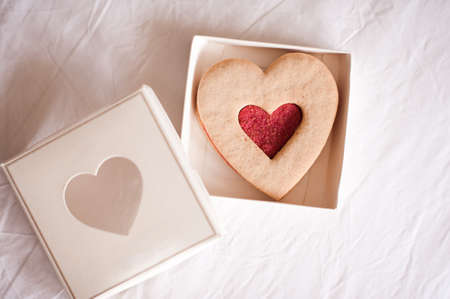 Tasty heart shape cookie with strawberry jam in pretty gift box closeup on table in kitchen.の写真素材