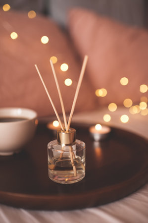 Home liquid perfume in glass bottle with sticks on tray with cup of tea in bed close up. Good morning. Cozy atmosphere conept.の写真素材