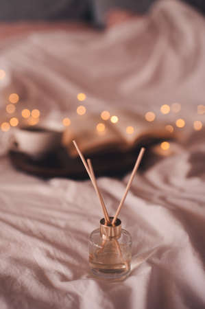 Liquid home perfume in glass bottle with sticks over glowing lights in bed at home close up. Cozy atmosphere concept. Freshness.の写真素材