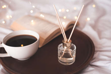 Cup of fresh black coffee with open paper book and liquid home perfume in glass bottle with sticks...