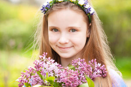 Smiling blonde teen girl 14-15 year old holding flowers over nature green background close up. Looking at camera. Childhood.の写真素材