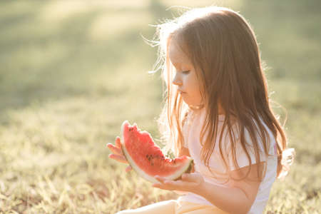 Cute baby girl 3-4 year old eating tasty watermelon over green nature background close up. Healthy lifestyle. Childhood. Summer time.の写真素材