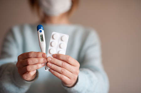 Aged adult woman holding digital thermometer with high temperature and meds at home close up. Health...