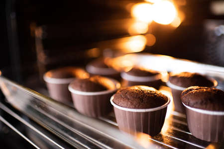 Open home oven with chocolate tasty muffins in bakeing forms on tray at home. Making fresh cupcakes in stove close up.の写真素材