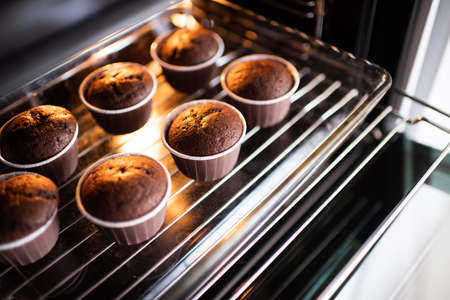 Open home oven with chocolate tasty muffins in bakeing forms on tray at home. Making fresh cupcakes...