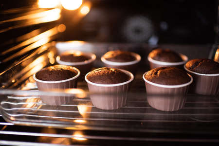 Open home oven with chocolate tasty muffins in bakeing forms on tray at home. Making fresh cupcakes in stove close up.の写真素材