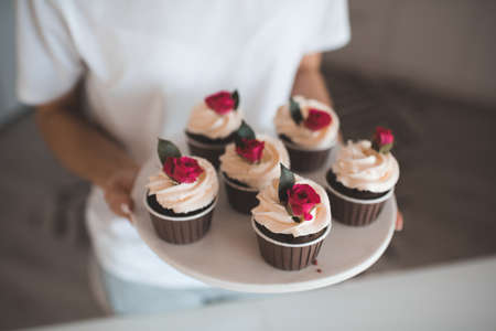 Woman bake cup cake with whipped crem icing and flower decoration in kitchen at home close up. Celebration.の写真素材