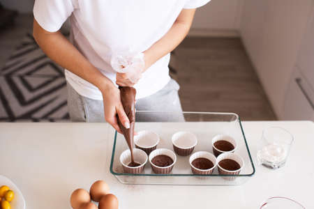 Woman making chocolate muffins at home. Put batter to cupcake forms in glass baking tray on kitchen...