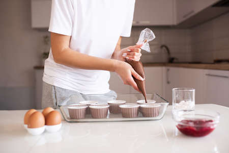 Woman making chocolate muffins at home. Put batter to cupcake forms in glass baking tray on kitchen table close up.の写真素材