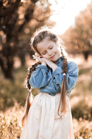 Smiling blonde kid girl 4-5 year old wearing casual trendy clothes resting over sunny natural background with cloed eyes. Childhood. Spring seson. Happiness.の写真素材