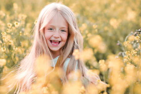 Smiling blonde cheerful kid girl 4-5 year old having fun in flower meadow over nature background...
