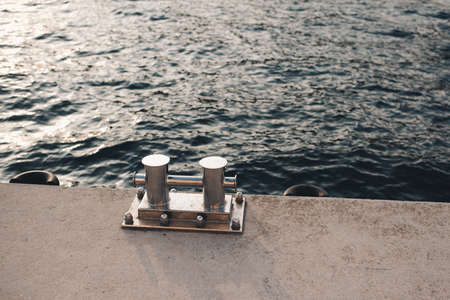 Metal bollard for boats and vessels on wharf over sea and sunset background close up. Maritime quayside with equipment for yatching at coastline. Travel season.の写真素材