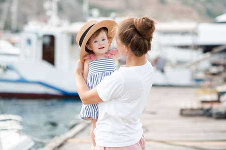 Mother with baby girl 1-2 year old with straw hat over sea and boats at background close up. Family lifestyle. Summer season. Childhood.の写真素材