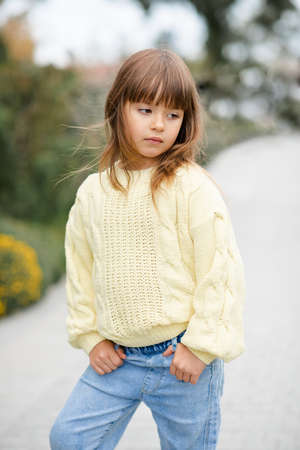 Stylish kid girl 5-6 year old wear trendy casual sweater and jeans pants walking in park outdoors. Springtime. Little child over nature spring background. Childhood.の写真素材