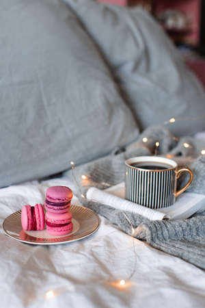 Cup of black coffee with paper book and burning candle with pink tasty macarons cookies in bed close up. good morning. Breakfast and leisure time.の写真素材