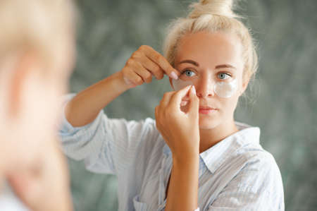 Beautiful woman put eye patches on face looking at mirror in room. skin health care.の写真素材
