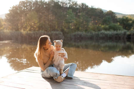 Smiling young mother playing with baby boy 1 year old wear casual clothes posing over nature background in sun light. spring season. motherhood. Happy and cheerful woman with child outdoor.の写真素材