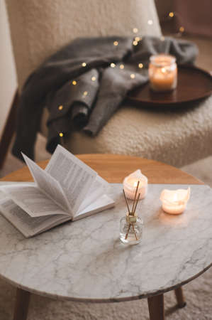 Liquid home fragrance in diffuser with open paper book on coffee table in bedroom indoors close up...