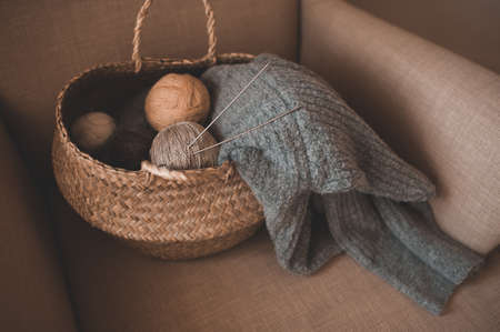 Making homemade knitted sweater at home. Straw basket with yarn wool skein with knitted fabric on...
