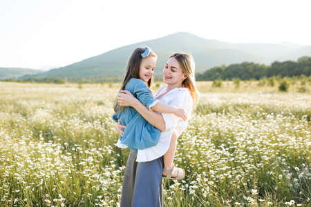 Cute beautiful young woman holding hands and play with little child girl walk in chamomile field...