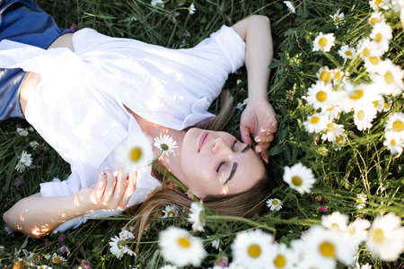 Beautiful adult girl relax in chamomile meadow with blooming flowers in nature top view. springtime....