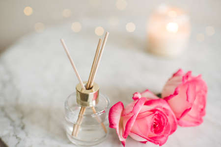 Liquid scented home fragrance in glass bottle and fresh rose flowers over burning candle and glow...