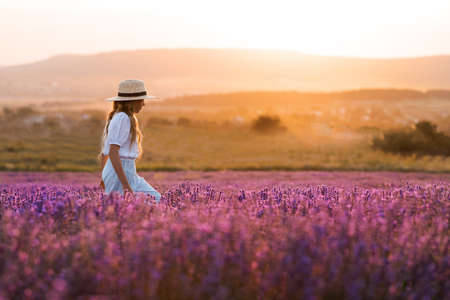 Stylish teenage girl 8-9 year old walking in blooming lavender flower field over nature sunny background outdoor. springtime.の写真素材