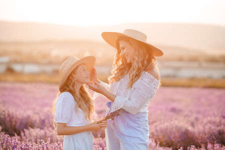 Smiling beautiful mother with kid girl 8-9 year old daughter wear straw hat stand in lavender flower field over sunset nature background. summer season. motherhood. happy woman with child together.の写真素材