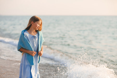 Stylish teenge kid girl 12-14 year old wear trendy dress and knit blue cardigan walk in sea beach coast outdoor. child over ocean. summer season.の写真素材