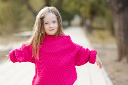 Cute funny child girl 4-5 year old wear bright pink sweater having fun playing in park outdoor. Childhood. autumn season.の写真素材