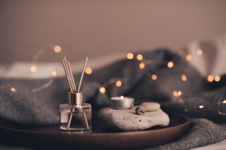 Liquid home fragrance with burning scented candle on stone tray over glow christmas lights at home close up. Cozy hygge atmosphere.の写真素材