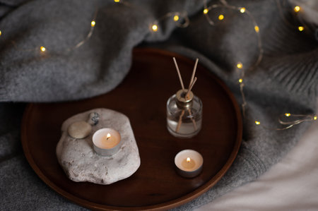 Liquid home fragrance with burning scented candle on stone tray over glow christmas lights at home...