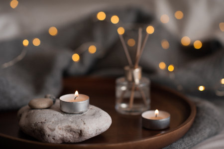 Liquid home fragrance with burning scented candle on stone tray over glow christmas lights at home close up. Cozy hygge atmosphere with candlelight.の写真素材
