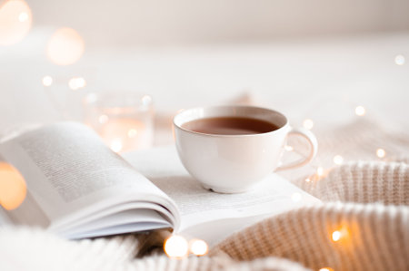 Open book with cup of coffee in bed with knit cloth sweater over glow christmas lights at background close up. good morning.の写真素材