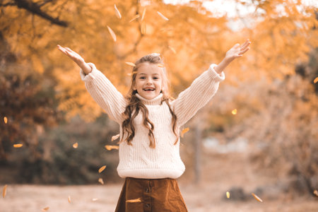 Smiling stylish child girl 5-6 year old wear knit sweater with yellow leaves over nature background outdoors. Happy little kid with blonde hairstyle. Childhood.の写真素材