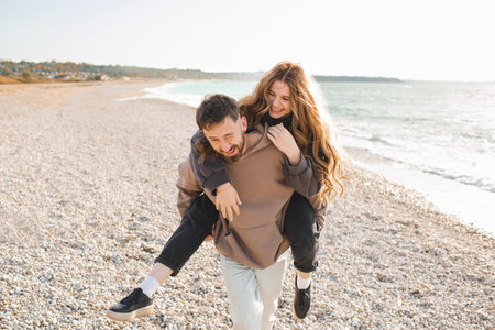 Happy young adults couple having fun at beach over sea background together. Smiling man carry pretty woman over ocean. Relationships.の写真素材