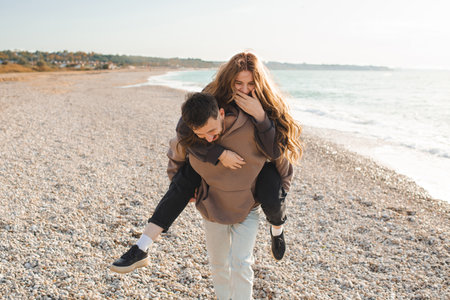 Happy young adults couple having fun at beach over sea background together. Smiling man carry pretty woman over ocean. Relationships.の写真素材