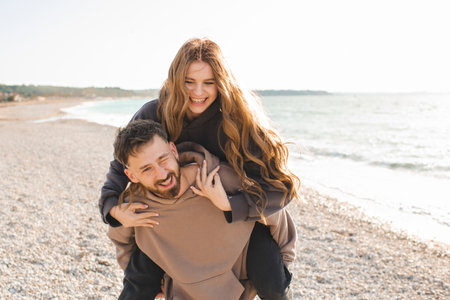 Happy young adults couple having fun at beach over sea background together. Smiling man carry pretty woman over ocean. Relationships.の写真素材