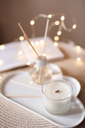 Home liquid perfume in glass bottle with bamboo sticks and scented candle on tray at coffee table in...