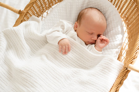 First days of little baby infant sleeping in straw crib wearing white pajamas at home top view....