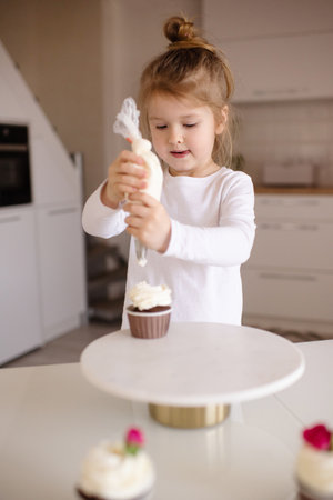 Cute funny baby girl 4-5 year old making cupcakes at kitchen table at home. Little child cooking cakes. Childhood.の写真素材