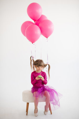 Cute happy child girl 4-5 year old wear princess dress posing with balloons having birthday party over white in room. Childhood.の写真素材