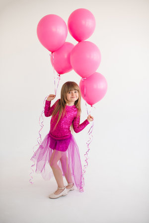 Cute happy child girl 4-5 year old wear princess dress posing with balloons having birthday party over white in room. Childhood.の写真素材